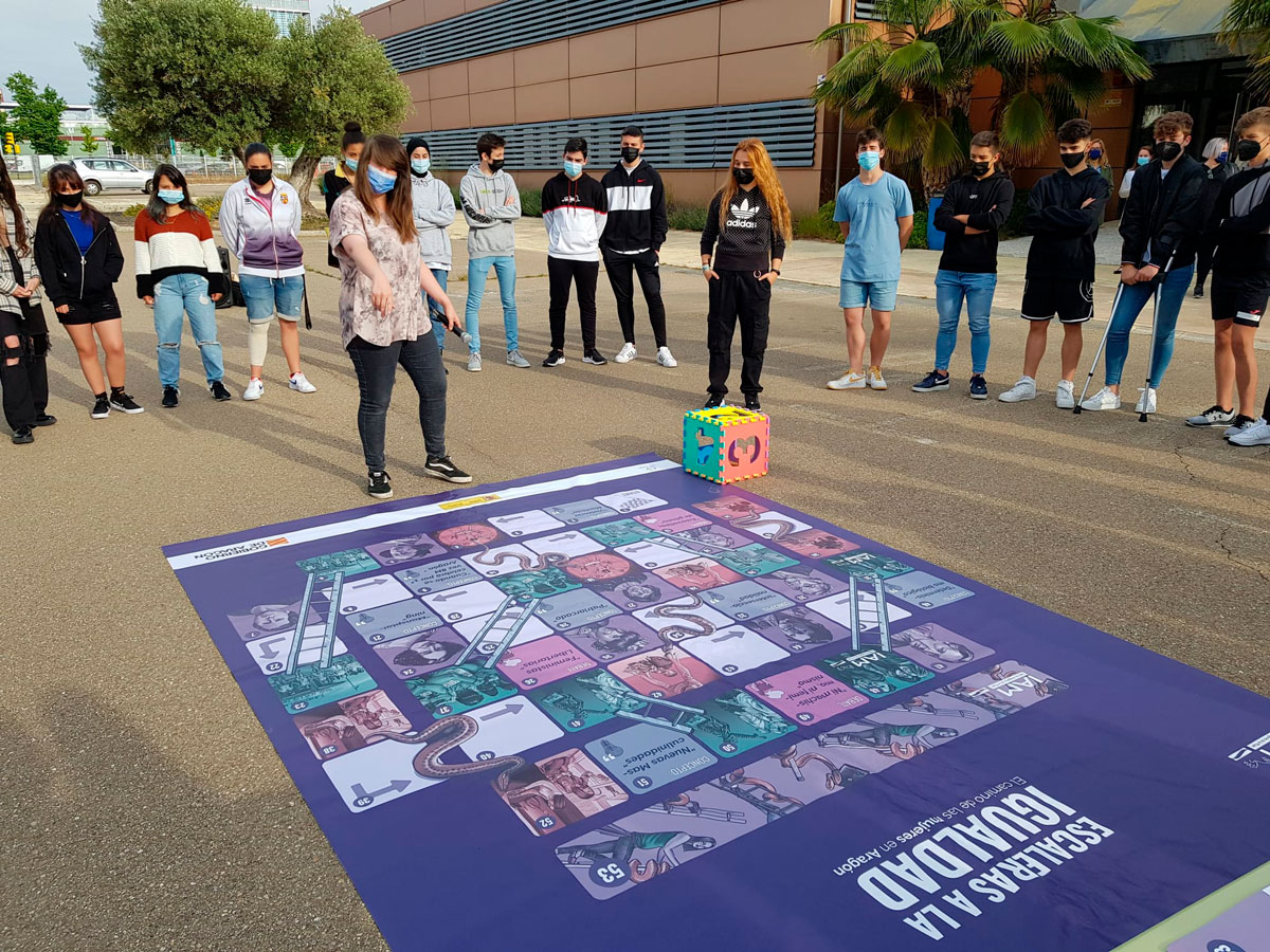 En esta imagen se observa la dinamización del juego "Escaleras a la igualdad" en un instituto de secundaria de Zaragoza. En esta dinamizaciones se contaba con un tablero de 5 metros que se extiende en el suelo como una alfombra.