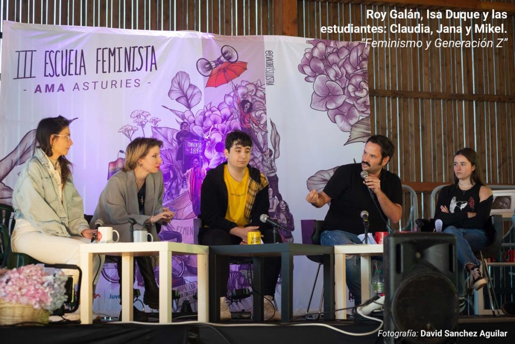 Roy Galán e Isa Duque, junto a tres estudiantes de bachillerato, durante su ponencia en la III Escuela Feminista AMA Asturies, con la gráfica de fondo de Eva Cortés Ilustra