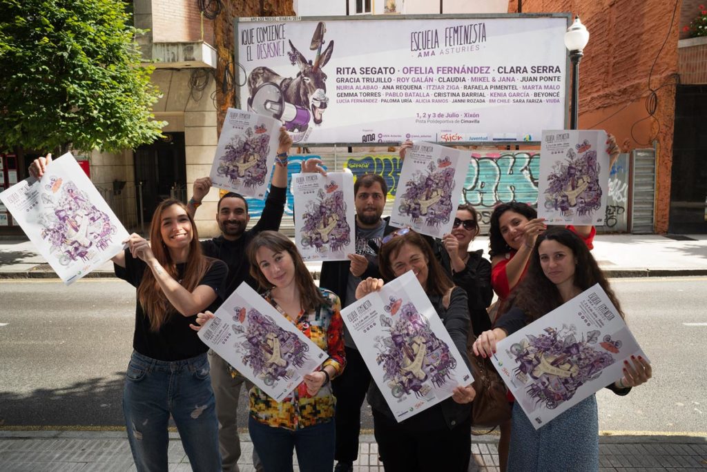 Miembros de AMA Asturies (Asamblea Moza d´Asturies) sujetando los carteles frente a una valla publicitaria a gran formato en una de las calles para entrar a Xixón.