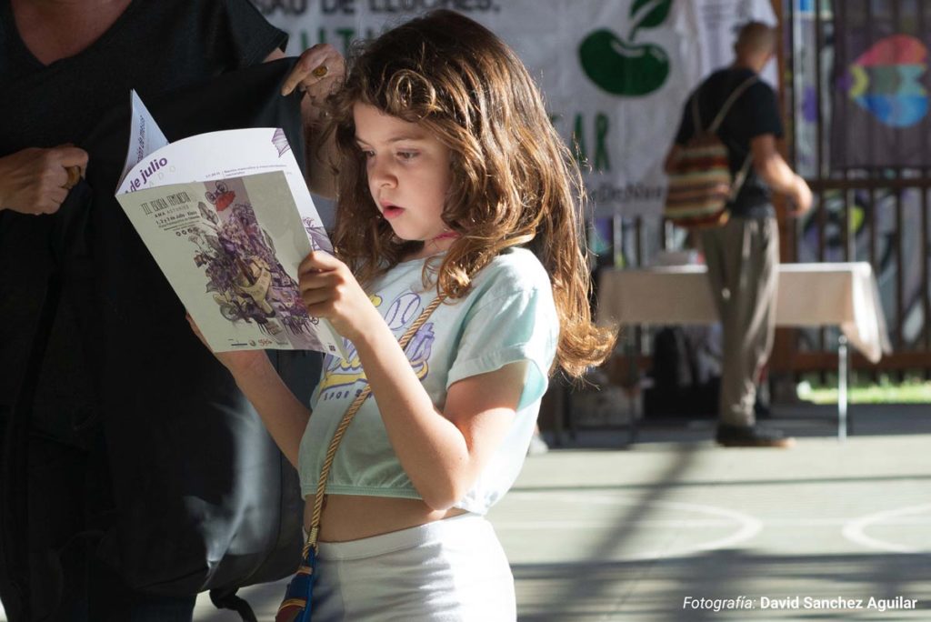 Niña sujetando y leyendo el libreto de la III Escuela Feminista de Ama Asturies, diseñado, maquetado e ilustrado por Eva Cortés