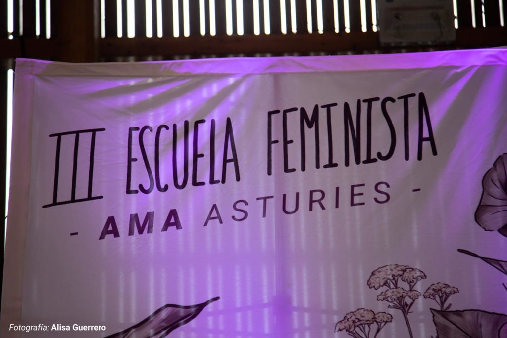 Lona del escenario con la ilsutración del cartel de la III Escuela Feminista de AMA Asturies y ilustrado y diseñado por Eva Cortés.
